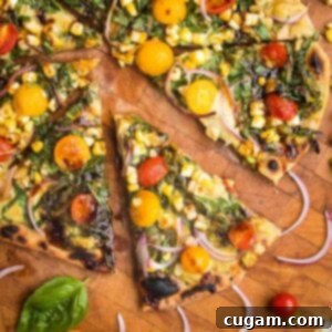 Flatbread Pizza with pesto, hummus, yellow and red tomatoes plus fresh basil and red onions. One slice shown up close and a few others partially shown on a wooden cutting board.