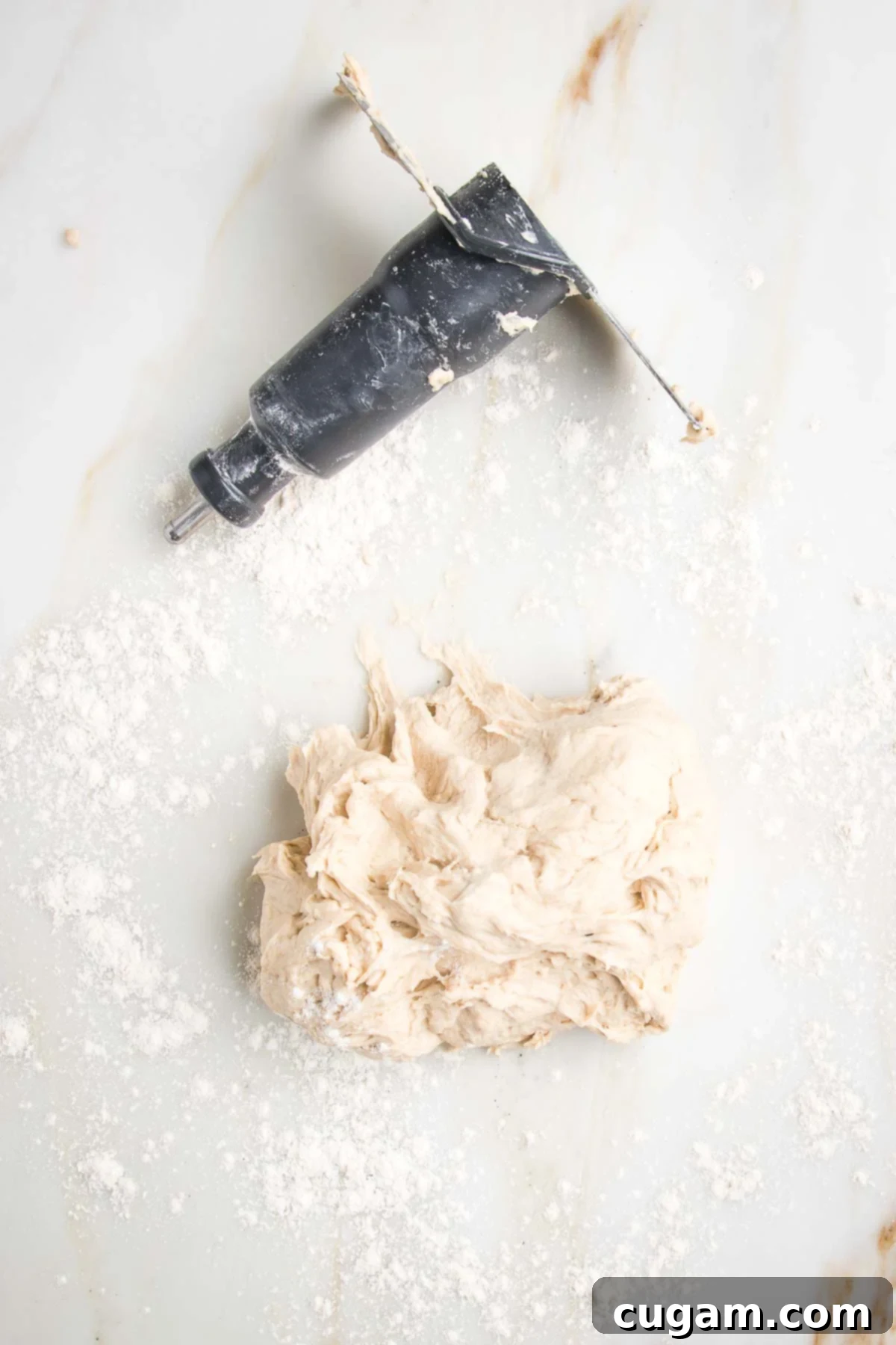 Ball of dough plus dough blade from a food processor on a lightly floured marble counter.