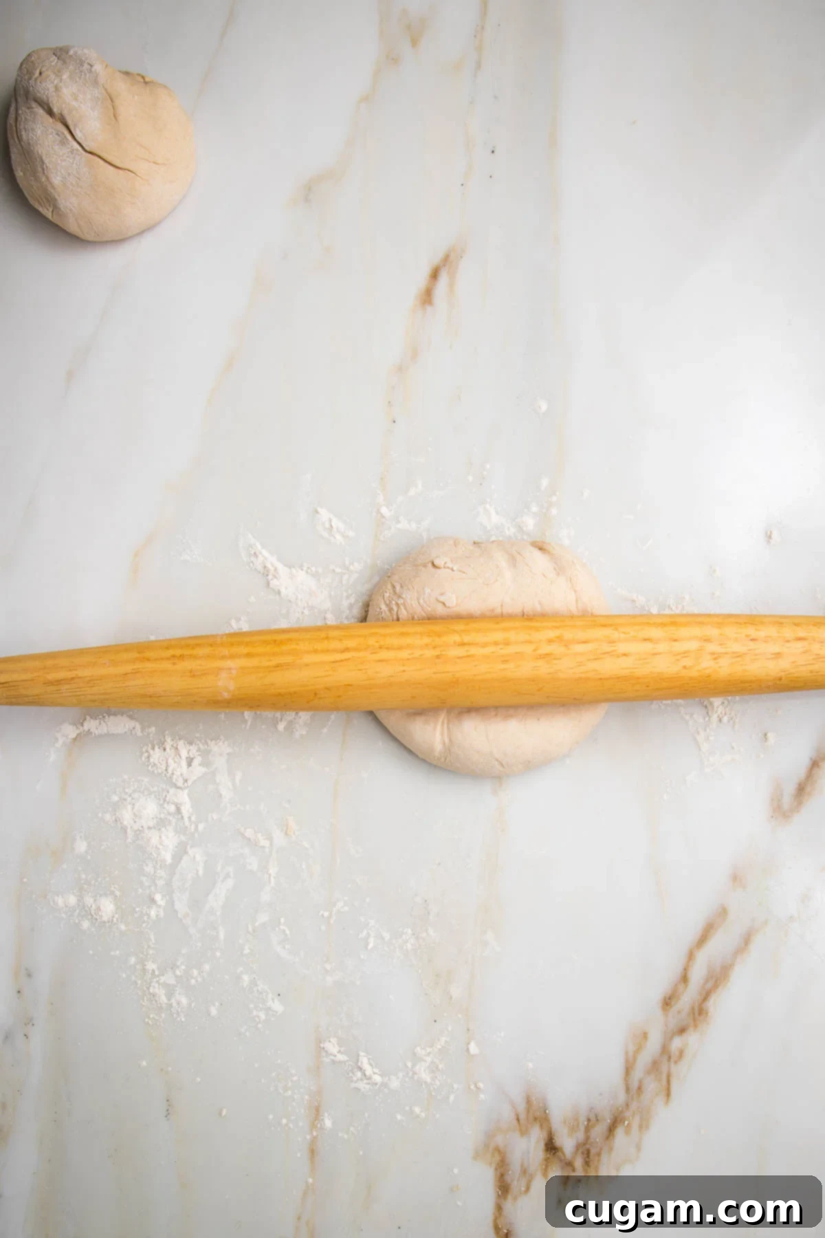 No yeast flatbread dough, split into two. Wooden rolling pin is rolling out one half of the dough.