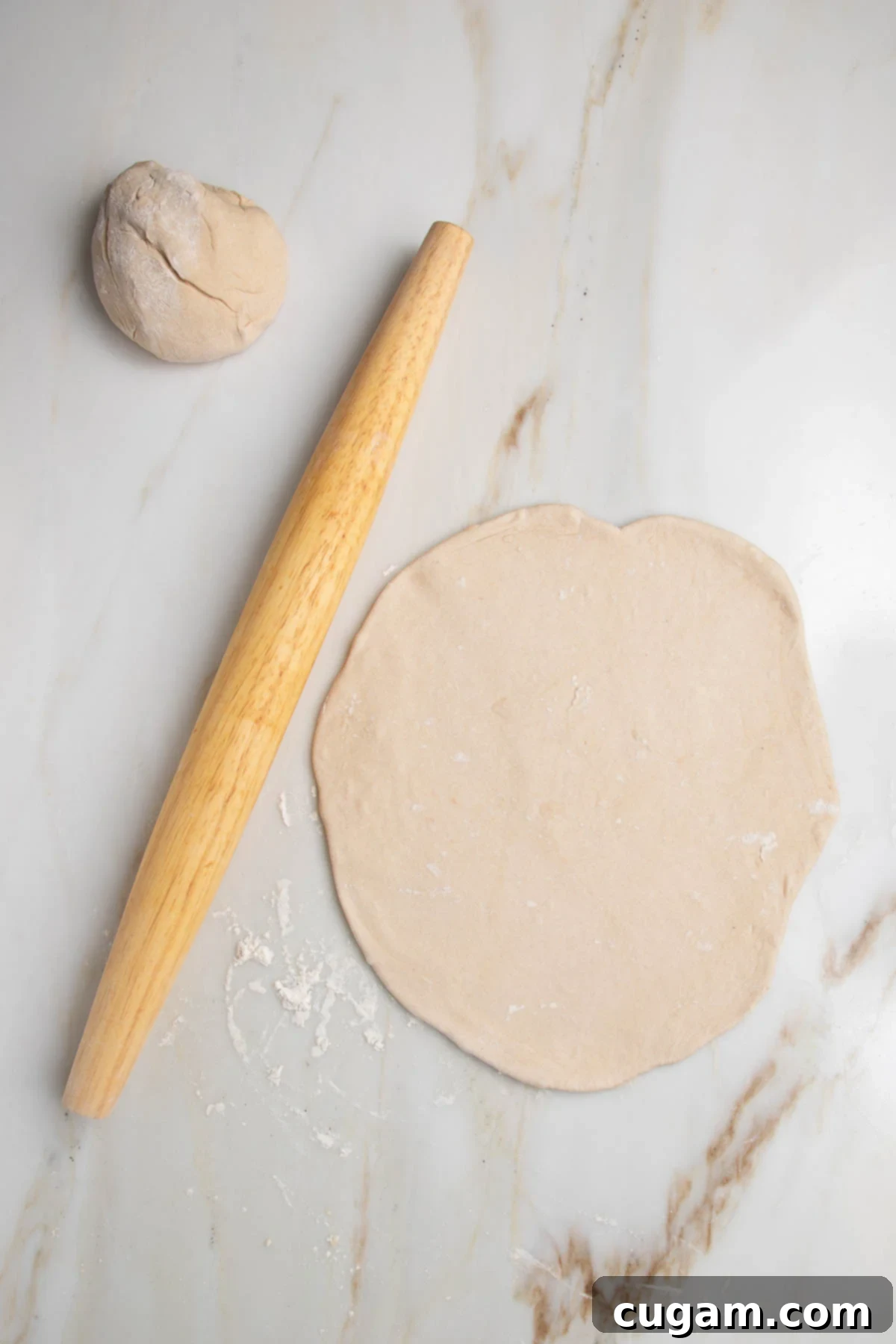 Ball of dough, wooden rolling pin and a flatbread dough rolled out into a circle.