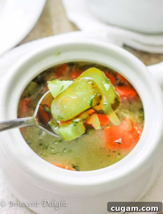 Polish pickle soup in a white bowl with a spoon lifting pickles