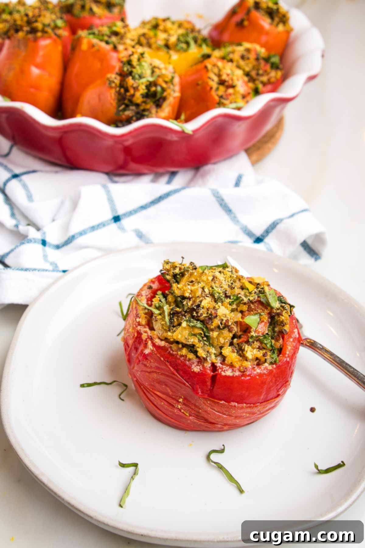 Baked stuffed tomato, sprinkled with fresh basil. In the background is a red pie dish filled more baked stuffed tomatoes.