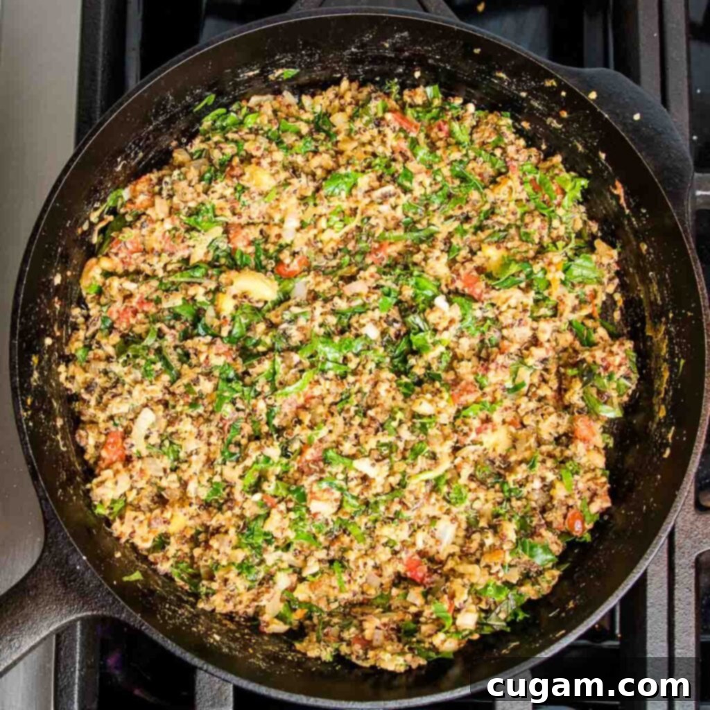 Cast iron skillet with sauteed veggies with quinoa, tomatoes and chopped greens. 