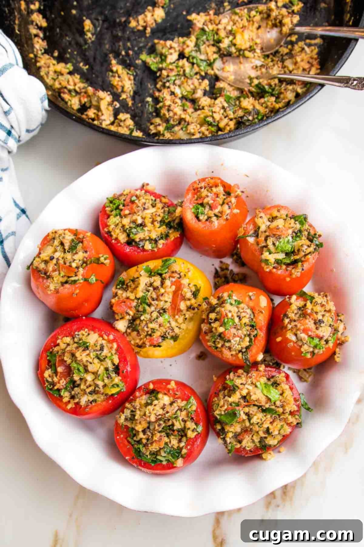 Baking dish with scooped out tomatoes, filled with quinoa stuffing. Cast iron skillet in the background with remaining filling. 