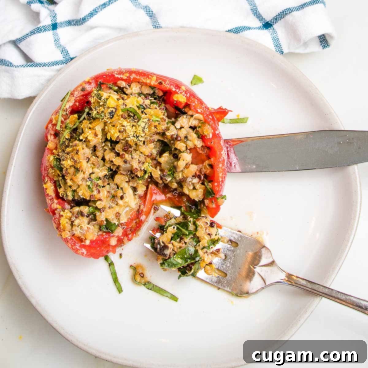 Baked stuffed tomato with quinoa, veggies and greens on a plate with a bite on a fork. 