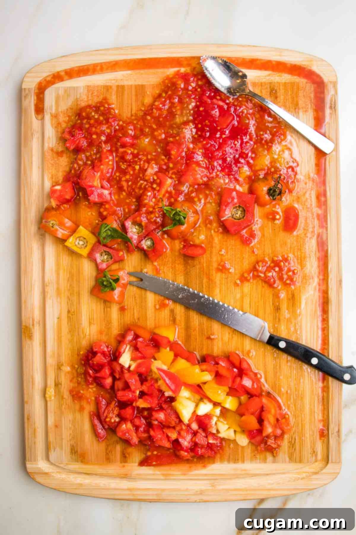 Wooden cutting board with juice rim. Tomato insides of pulp, juice and seeds. Pulp is cut into dice on the bottom. There is also a tomato knife and grapefruit spoon on the board.