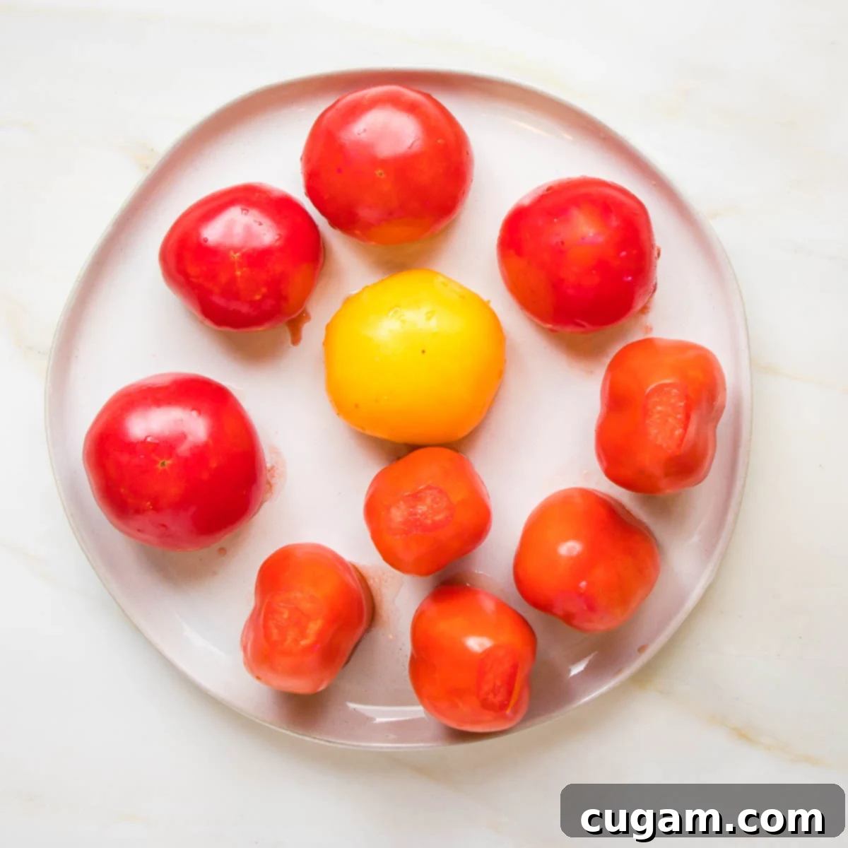Tomatoes with their tops cut off, placed upside down on a plate to drain.