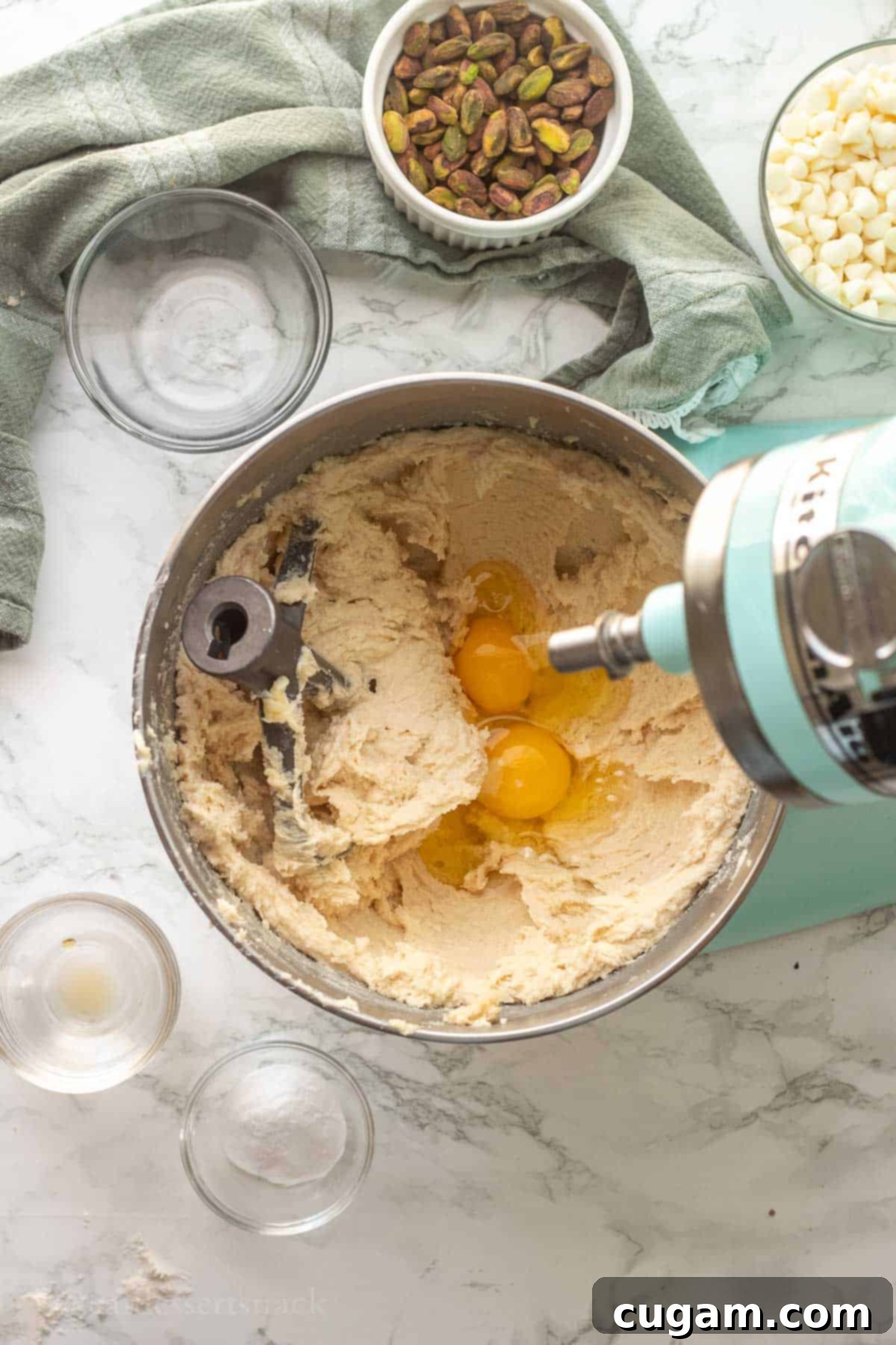 Two eggs being added to the creamed butter and sugar mixture in a mixing bowl, with a cookie mixing paddle.