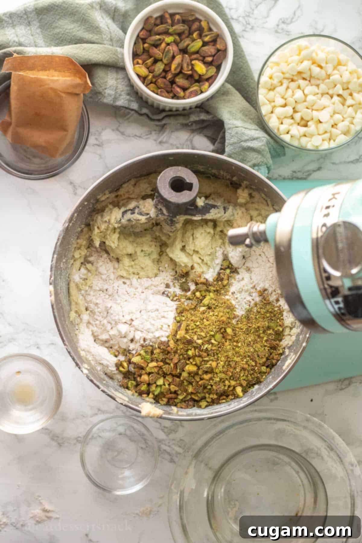 Chopped pistachios and flour being mixed into the pistachio cookie dough in a mixing bowl.