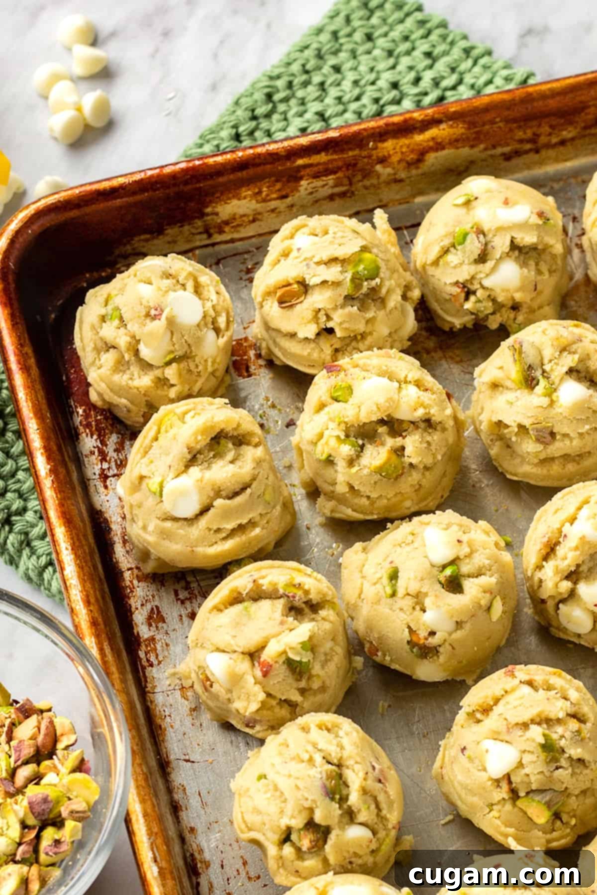 Raw cookie dough balls, scooped evenly, arranged on a metal baking sheet with a green hot pad underneath.