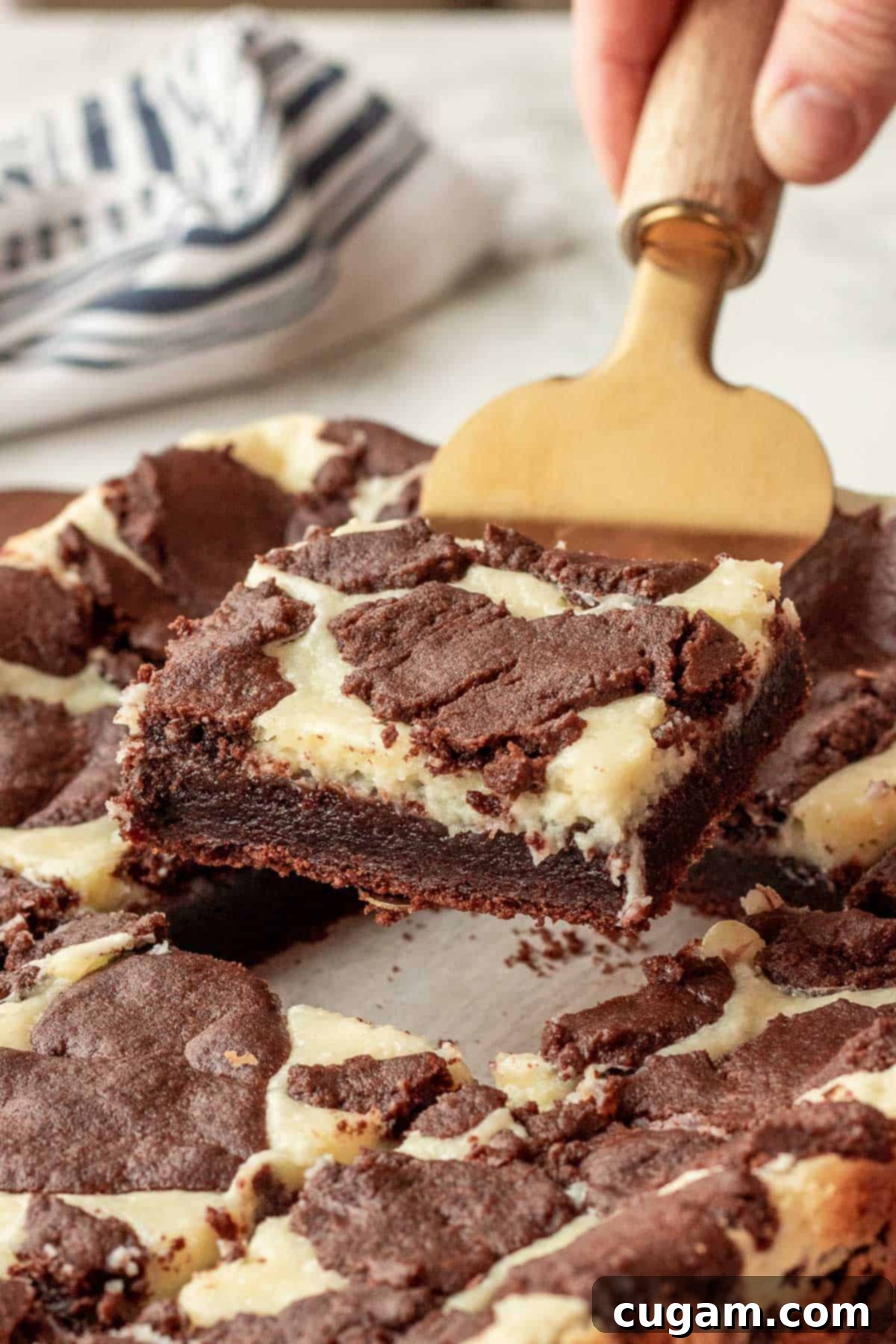 A perfectly baked Brownie Cheesecake Bar slice resting on a gold spatula, showing the distinct layers of brownie and creamy cheesecake.