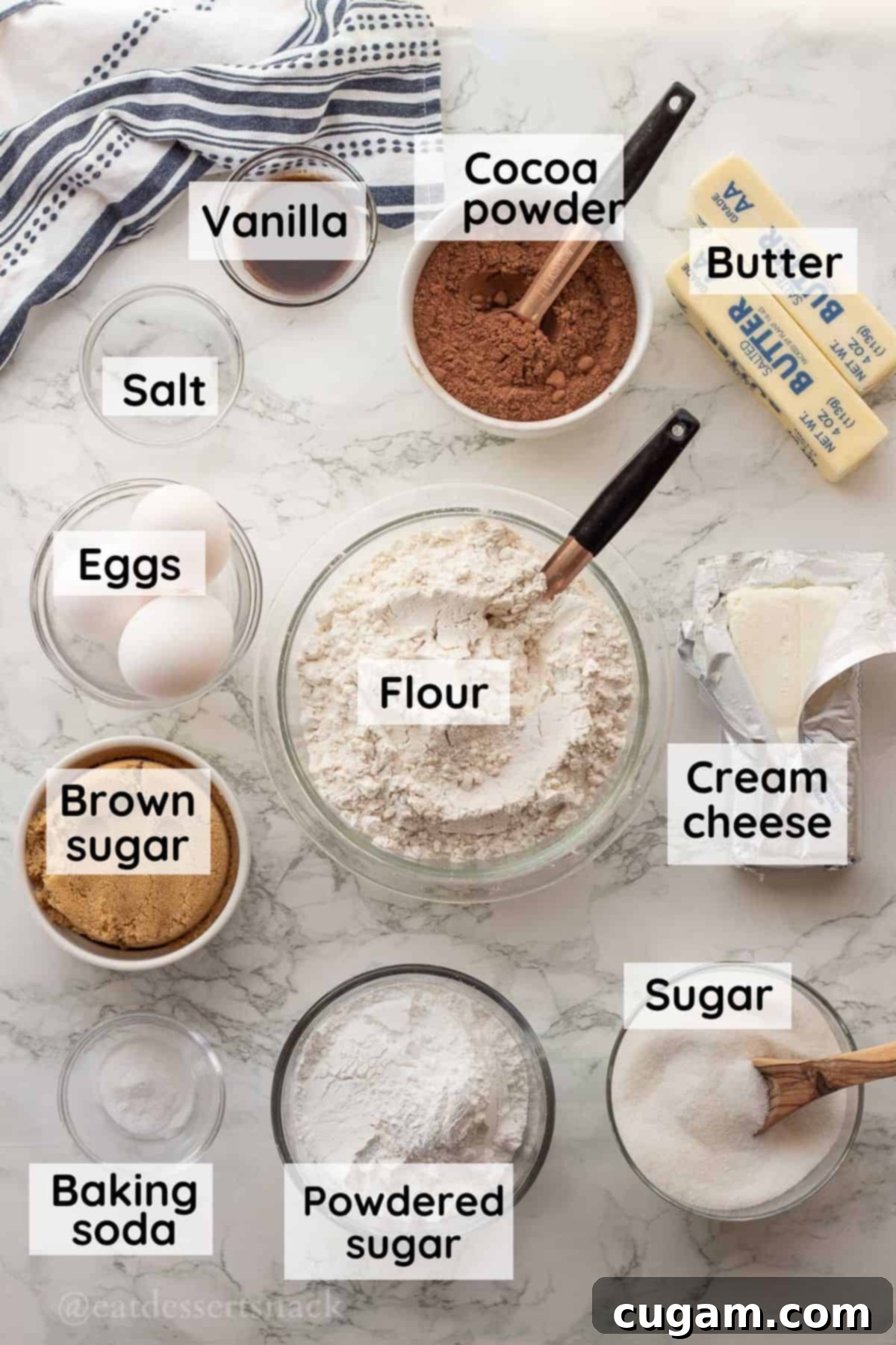 Various baking ingredients including cocoa powder, butter, vanilla extract, eggs, salt, cream cheese, sugars, and flour, arranged in glass bowls on a marble countertop.