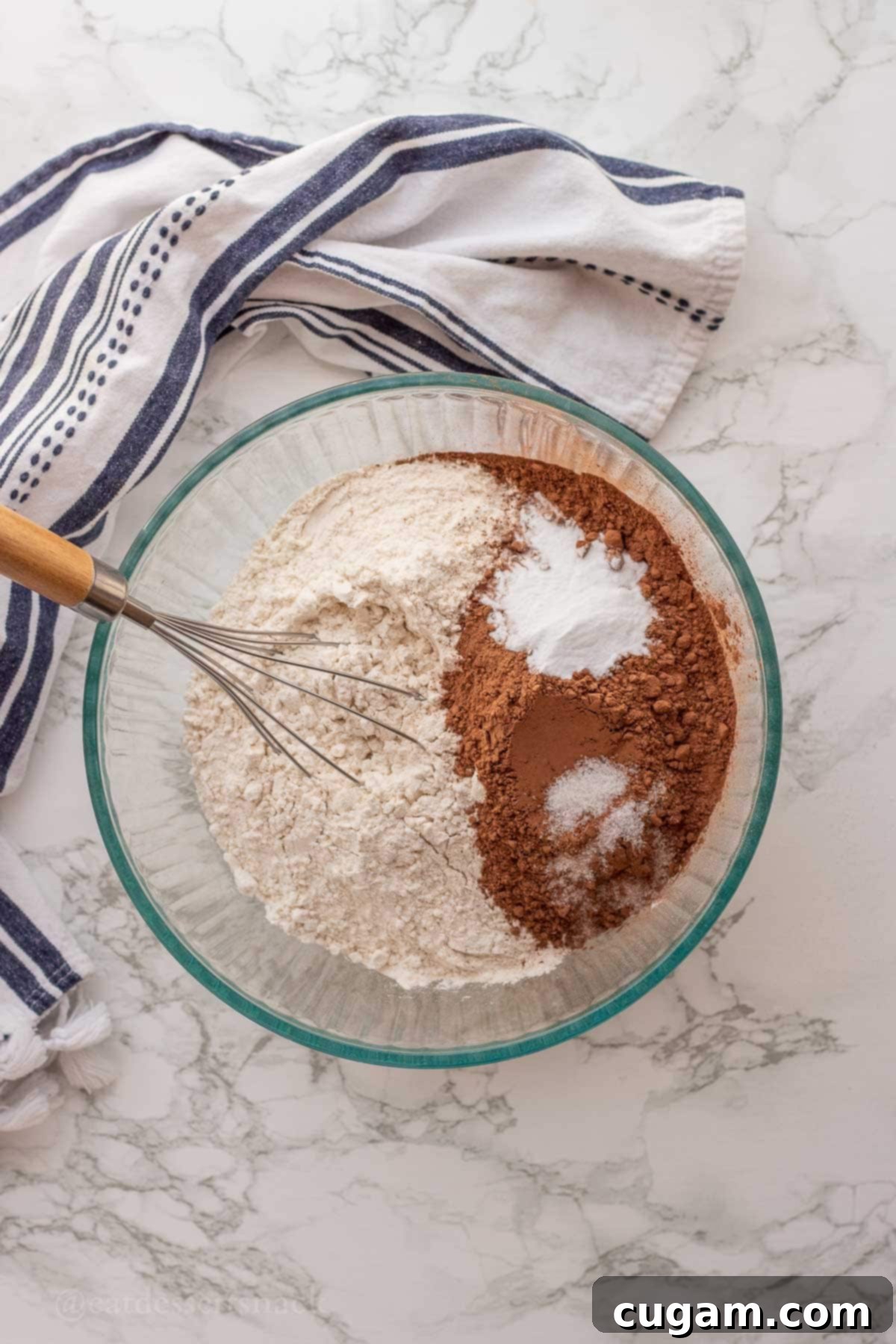 Dry ingredients including flour, salt, baking soda, and cocoa powder in a glass bowl with a whisk, ready to be combined.