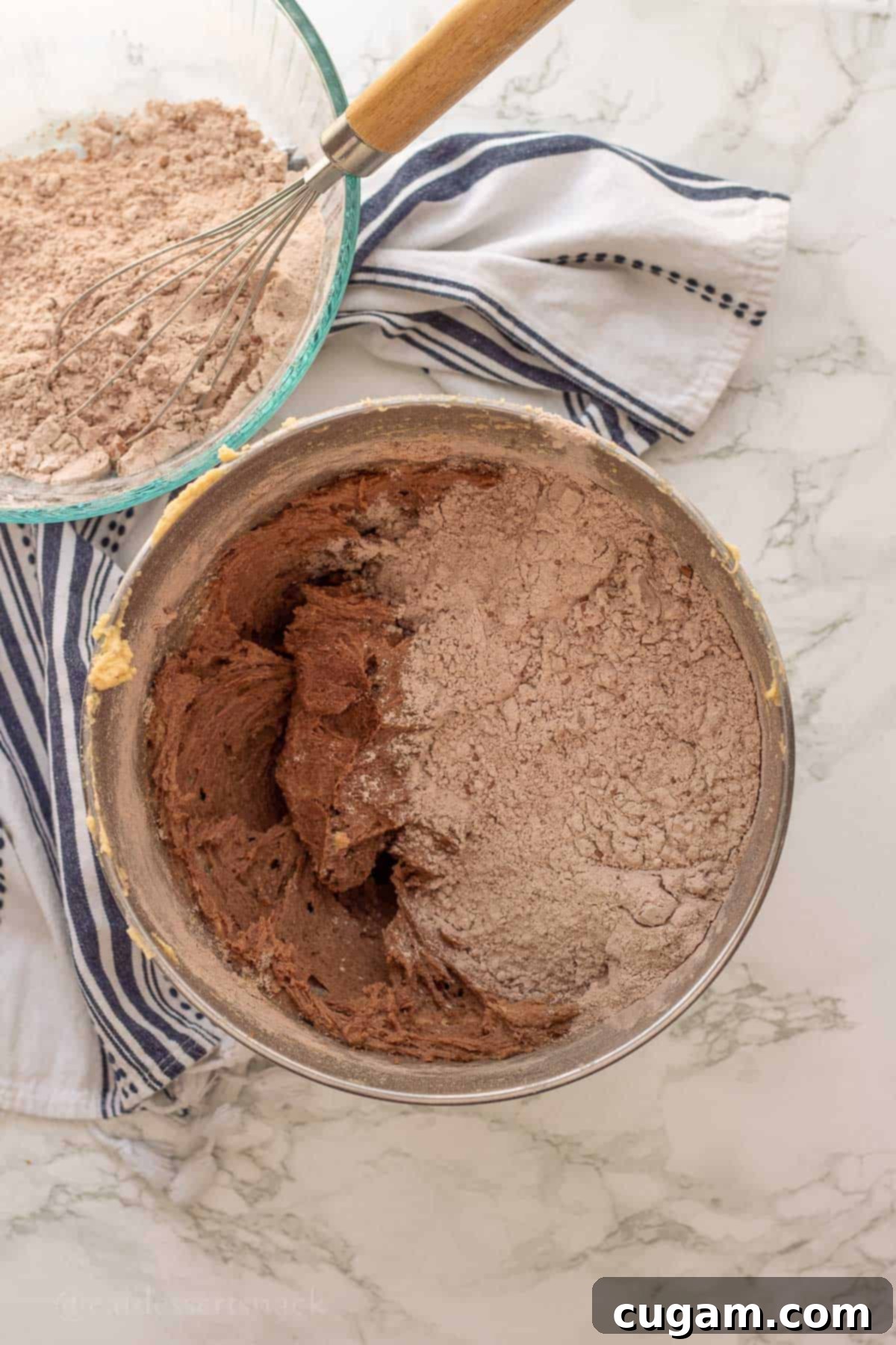 The dry flour mixture being gently folded into the wet butter mixture in a metal bowl, creating raw brownie batter.