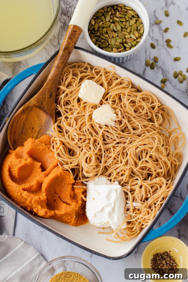 Ingredients for Creamy Pumpkin Pasta Sauce: butter, pumpkin puree, wooden spoon, and cream cheese laid out on a surface.