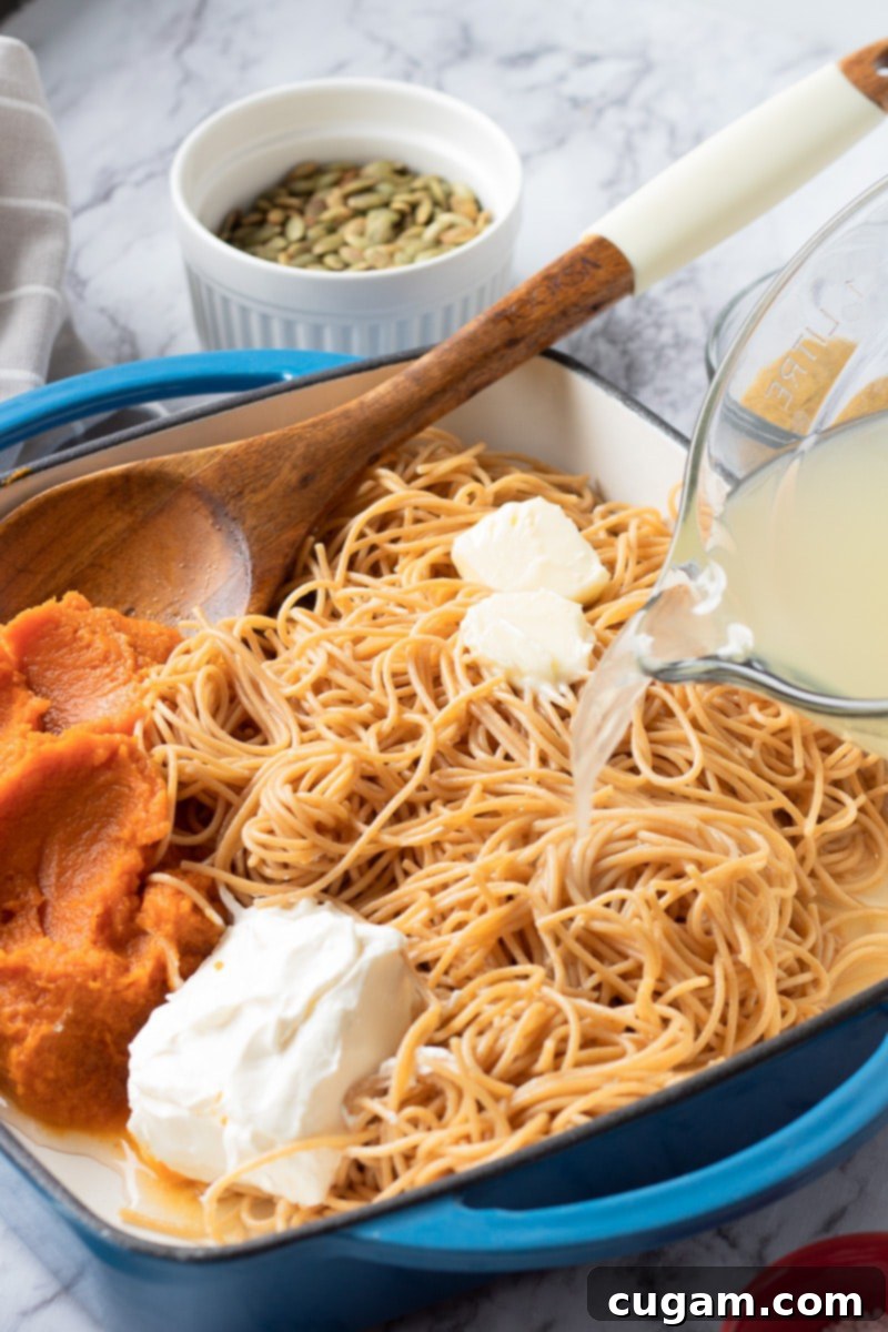 Pouring reserved pasta water into a pan with noodles, cream cheese, pumpkin puree, and butter, to create the sauce.