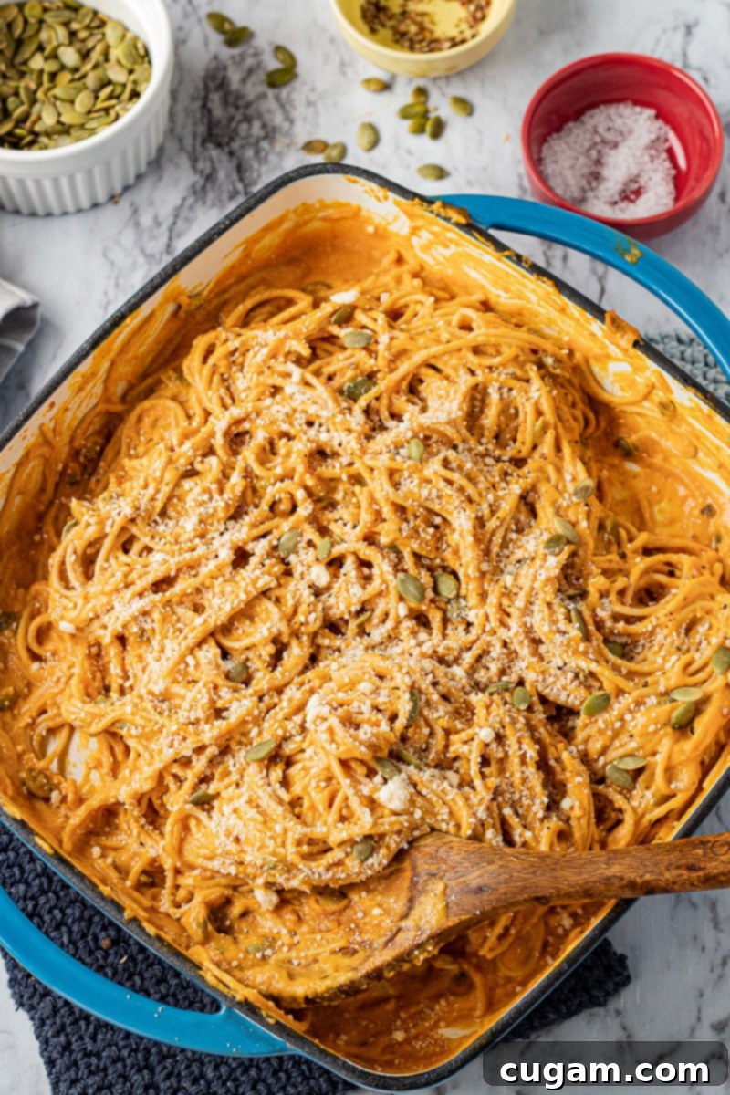 Cooked creamy pumpkin pasta in a square blue cast iron pan with a wooden spoon, ready to serve.