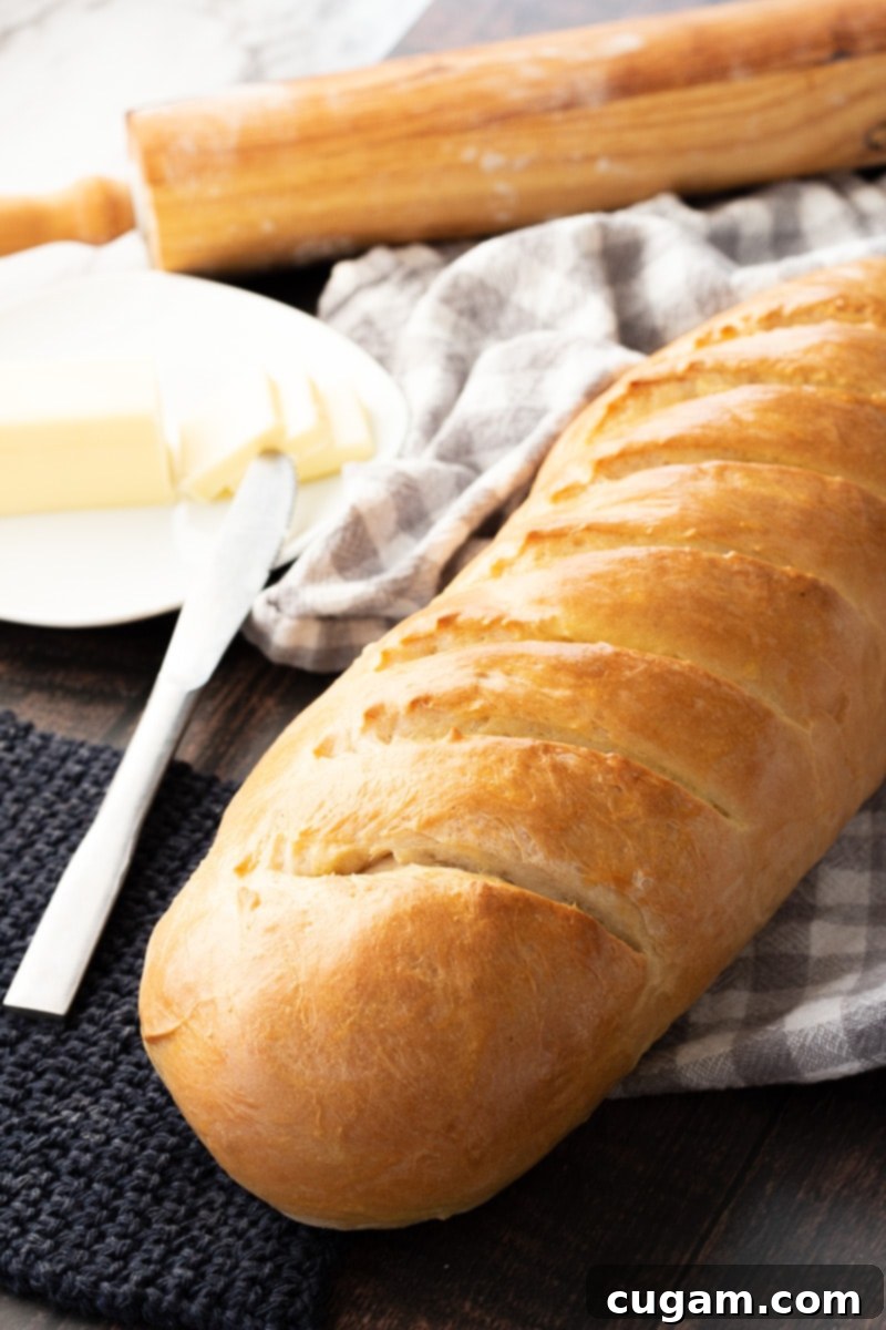 Baked crusty French bread on a dish towel with butter and rolling pin.