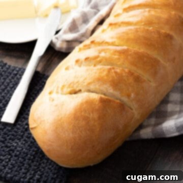 Baked loaf of fluffy french bread on wood table with towel, butter, and knife.