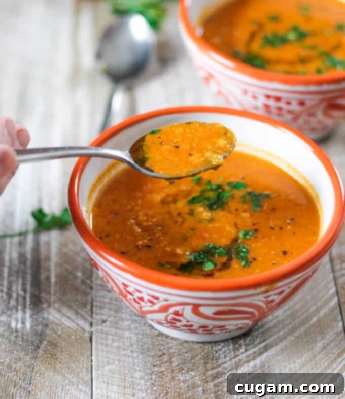 Tomatoes Red Lentils Coconut Soup on a spoon and in orange bowls, highlighting its vibrant color and creamy texture
