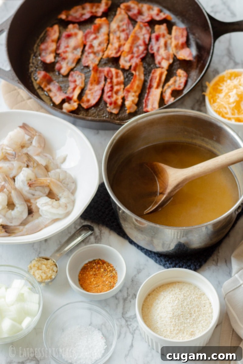 Ingredients for Cheesy Grits and Shrimp laid out on a marble counter: chicken broth, raw shrimp, grits, bacon in a cast iron pan, cheddar cheese, chopped onions, and salt.