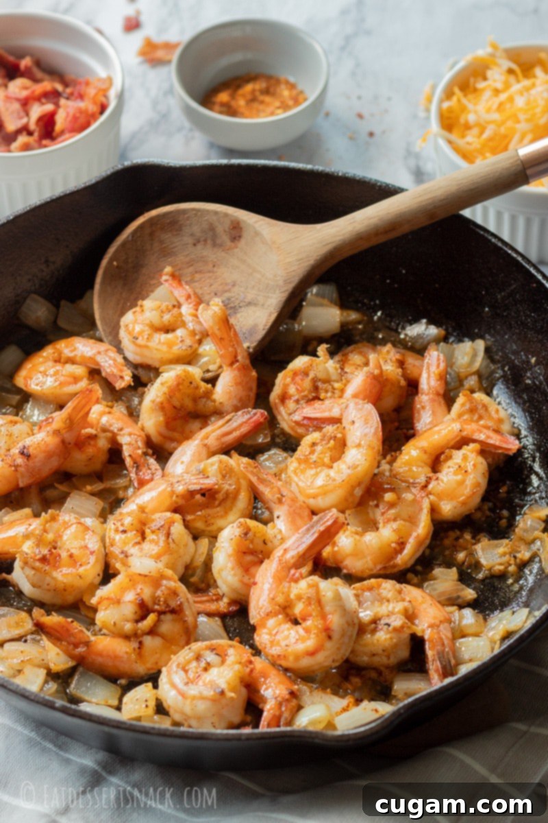 Cooked shrimp and slightly caramelized onions in a cast iron pan with a wooden spoon, ready to be served.