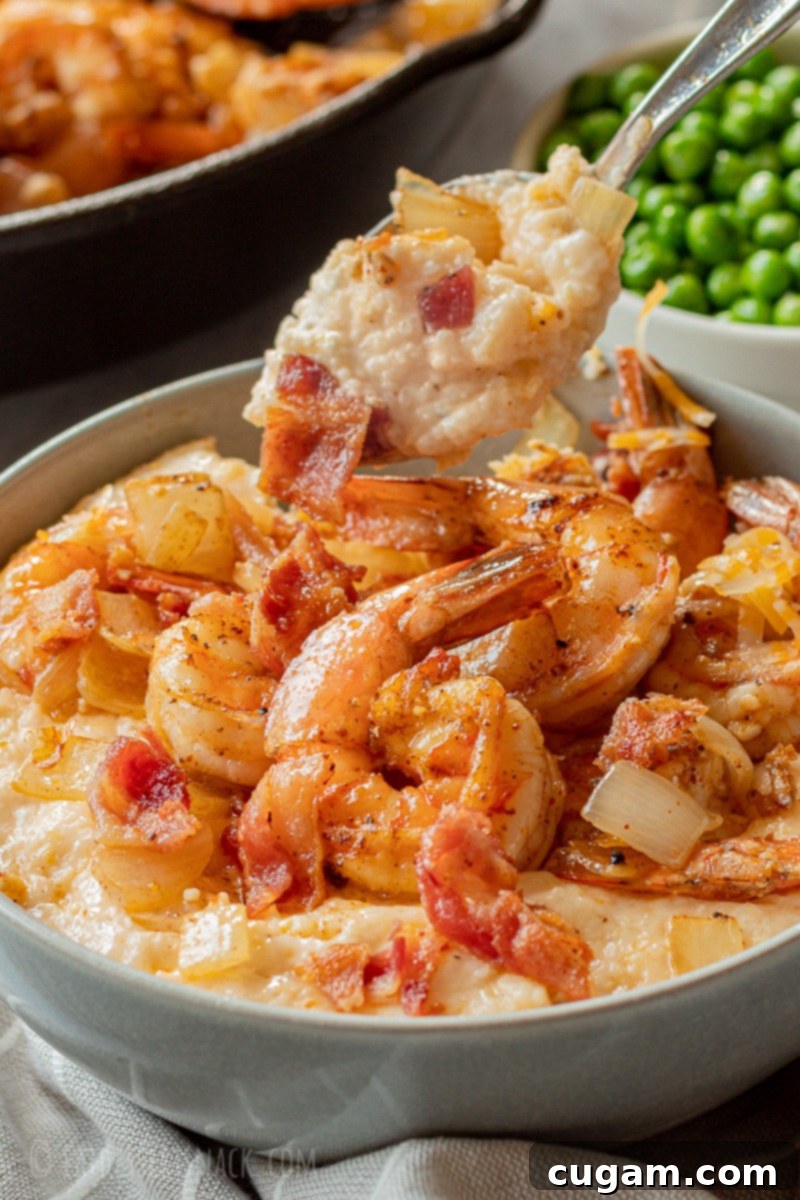 A spoonful of creamy, cheesy grits being lifted above a bowl filled with cooked grits, shrimp, and bacon.