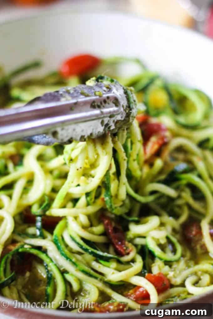 Zucchini noodles, pesto, and cherry tomatoes tossed together in a pan, glistening with olive oil.