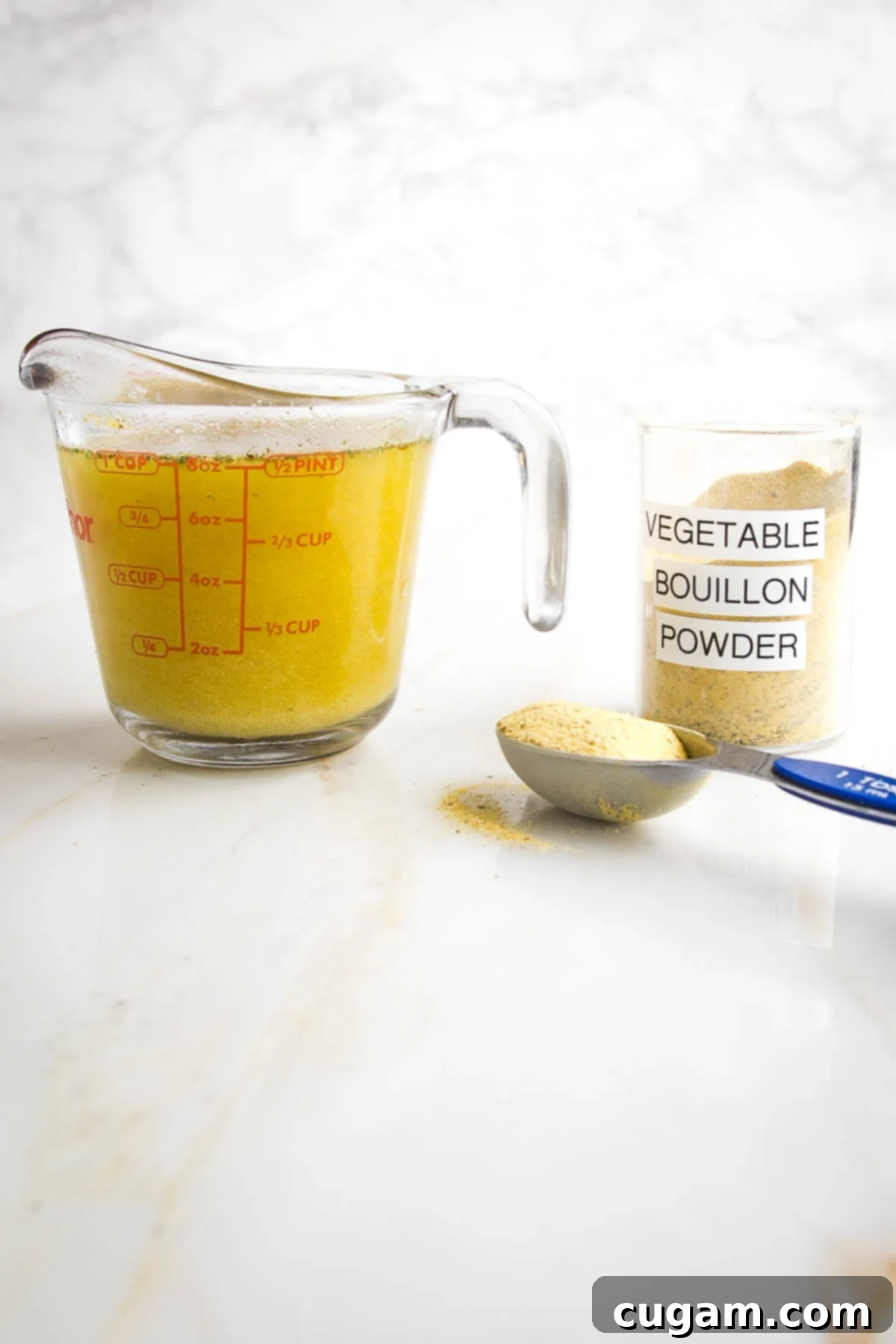One cup measure of vegetable broth next to a Tablespoon of bouillon powder from a jar marked as such.