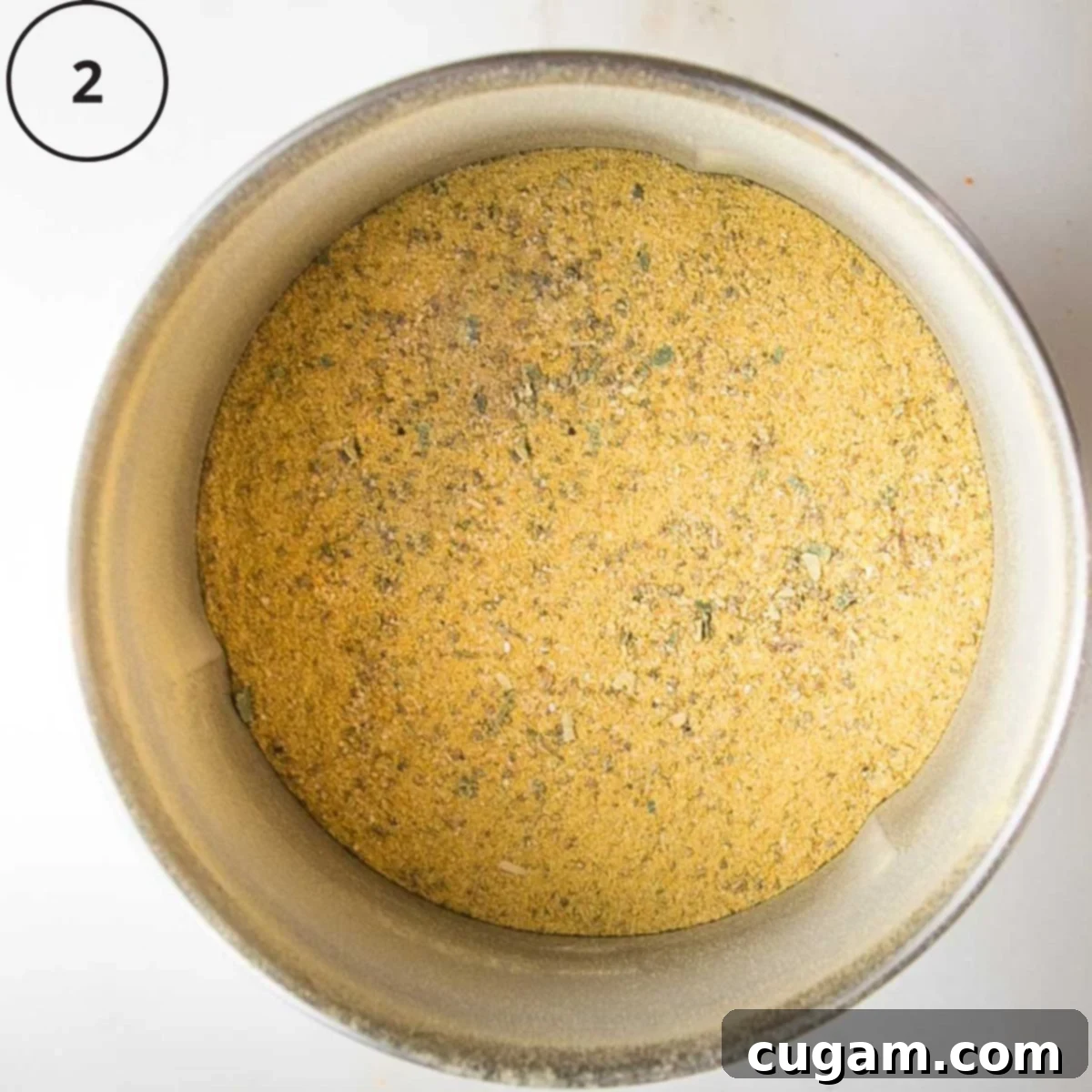 Yellow powder in a spice blender, speckled with green herbs.