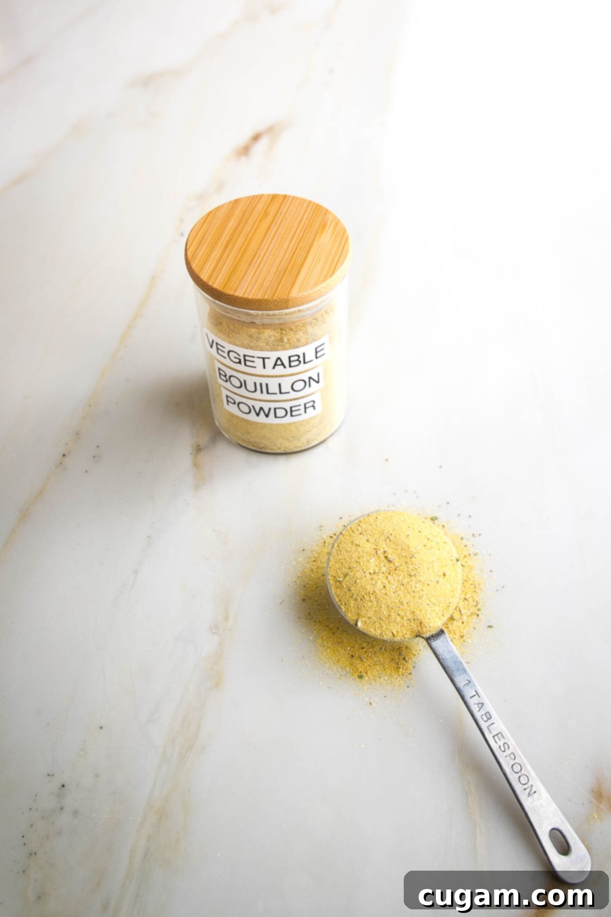 Vegetable Bouillon Powder labeled on jar with yellowish powder. A Tablespoon with same yellow spice mixture in the foreground.