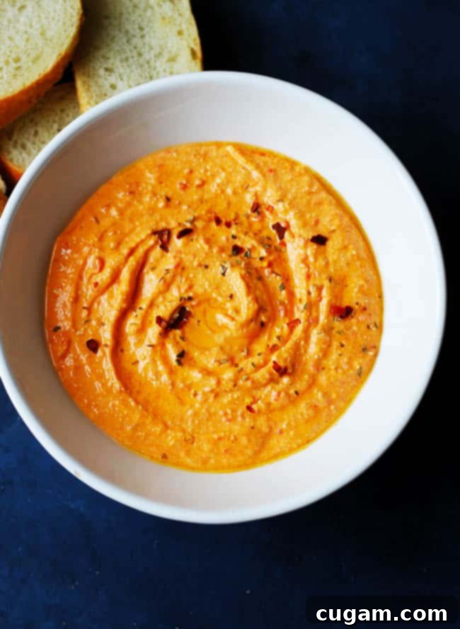 A close-up view of a white bowl filled with freshly made Tirokafteri (Spicy Feta Dip), garnished with a drizzle of olive oil and a sprinkle of red pepper flakes, ready for serving.