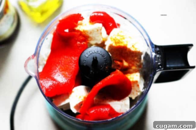 A food processor bowl filled with the initial ingredients for Greek Spicy Feta Dip: chunks of feta cheese, roasted red peppers, and red wine vinegar, before blending.
