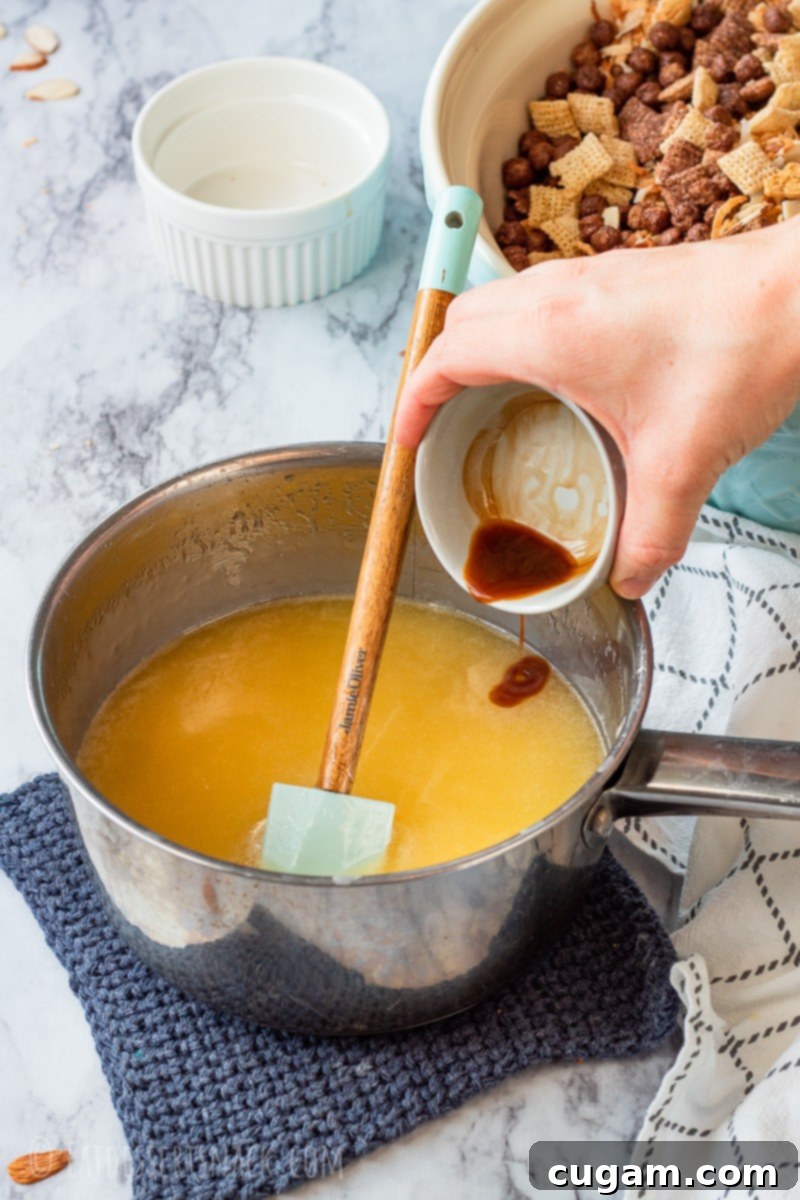 A small dish of clear vanilla extract being poured into a bubbling saucepan containing the corn syrup, sugar, and butter mixture, highlighting the addition of a key flavor enhancer.