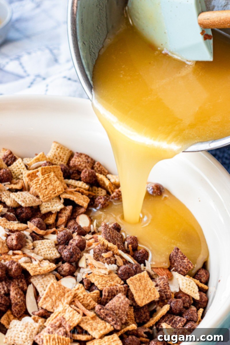 A close-up view of the gooey cooked corn syrup, butter, and sugar mixture being poured directly from a saucepan into a large bowl filled with mixed cereals, ready to be coated.