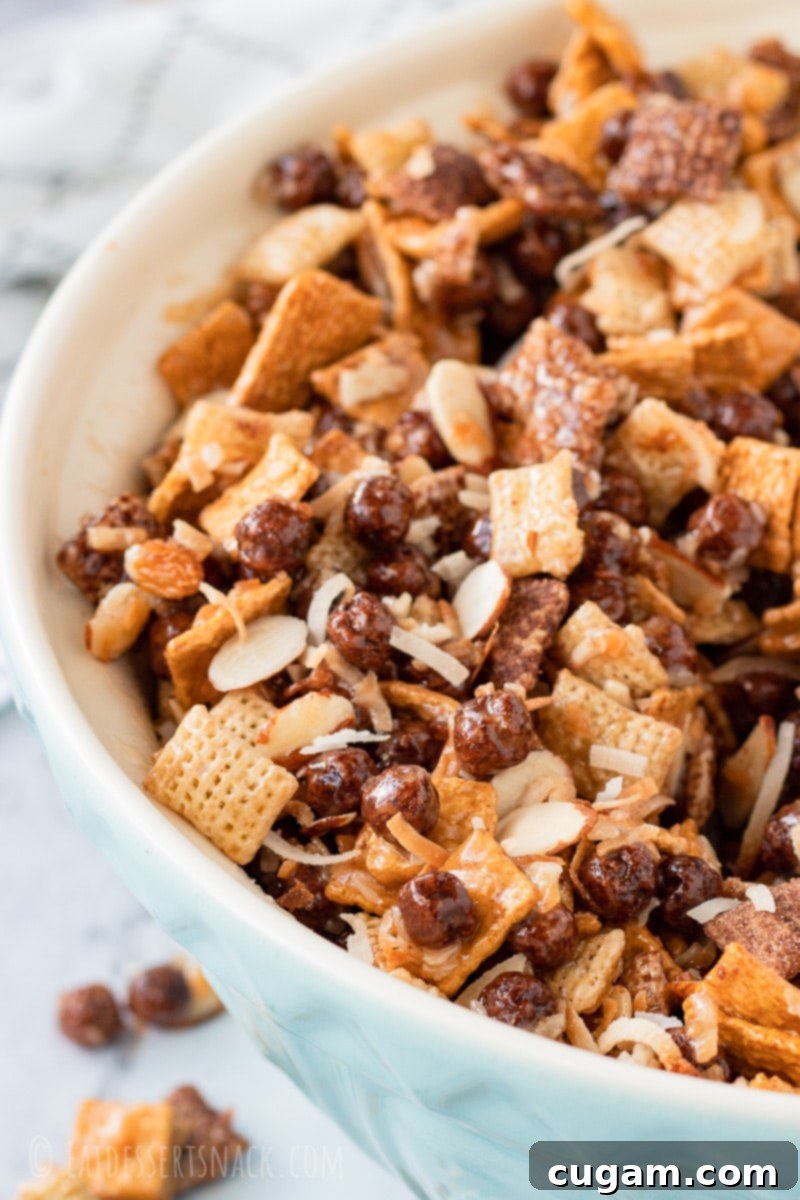 A vibrant blue bowl generously filled with Chocolate Gooey Chex Mix, showcasing its enticing texture and delightful mixture of ingredients, ready to be enjoyed.