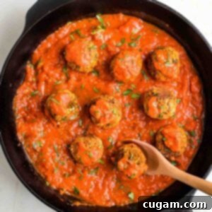 Cast iron skillet filled with marinara sauce and vegan meatballs.