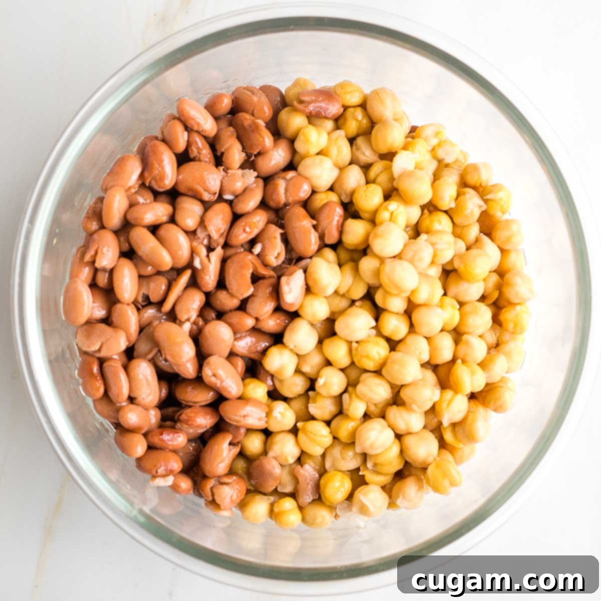 Pinto beans and chick peas in a glass mixing bowl, ready to be mashed.