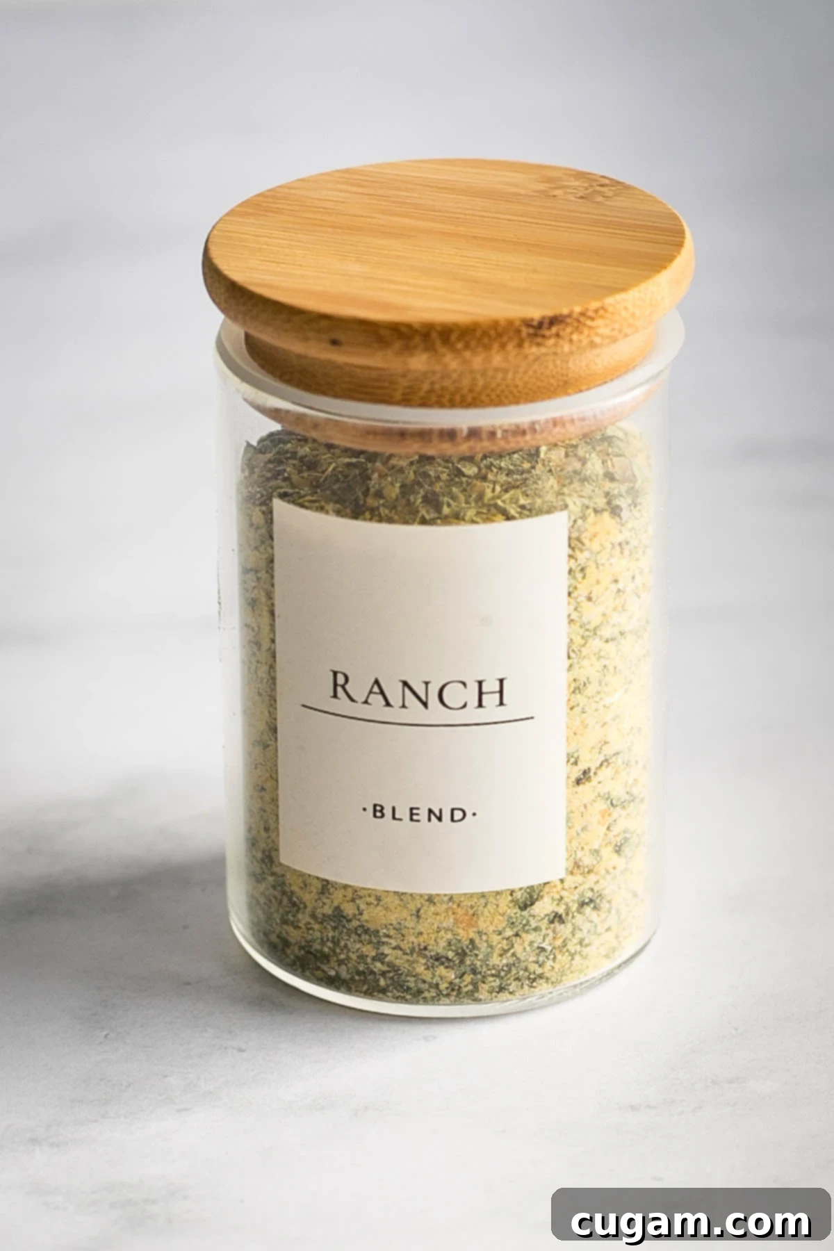 Small spice jar labeled "ranch blend" with a wooden stopper, loaded with dry ranch packet mix. The label clearly reads "Ranch Blend" against a backdrop of fresh ingredients and spices, showcasing the simplicity and natural origins of the mix.
