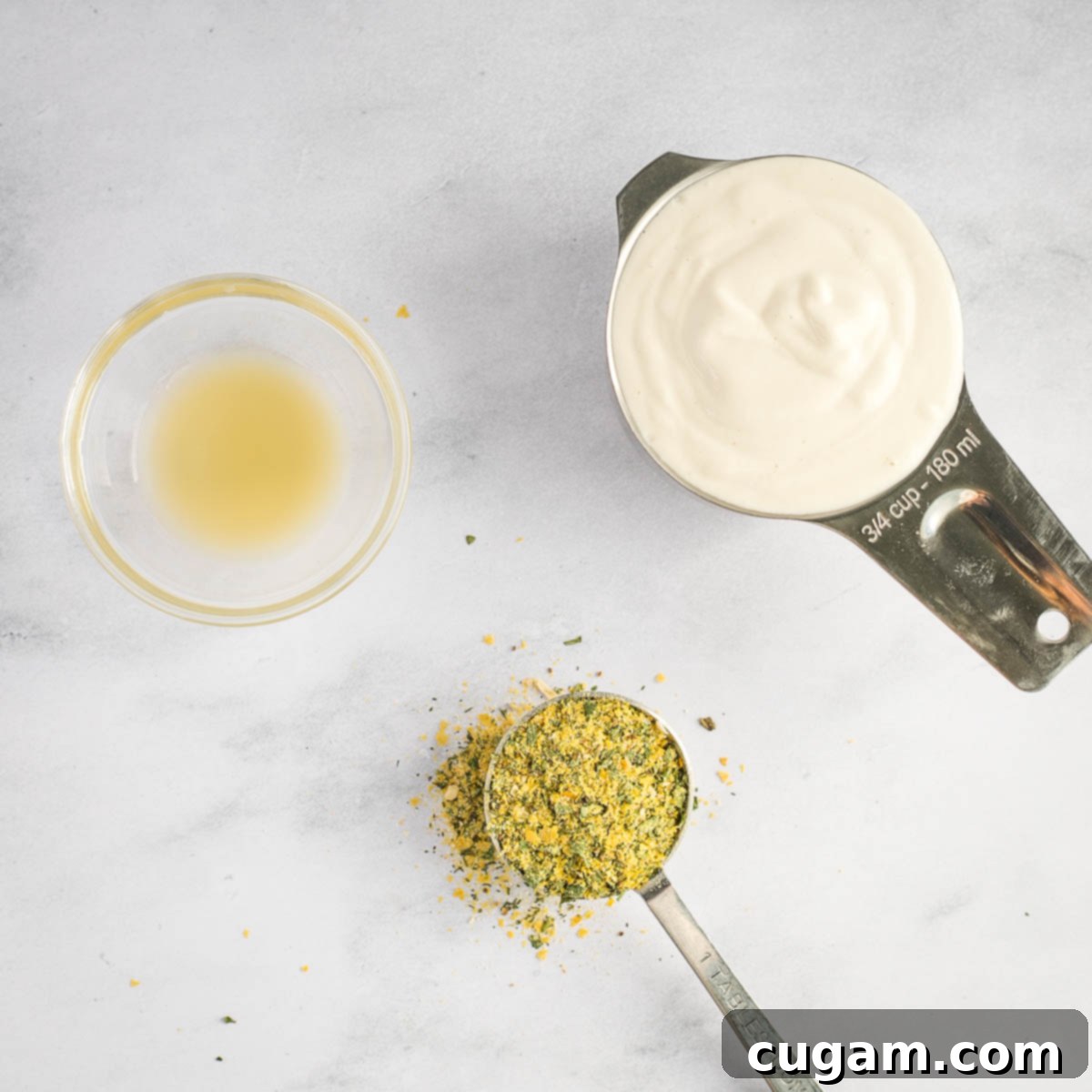 Dry measuring cup with vegan sour cream, a tablespoon of dry ranch mix, and a teaspoon of lemon juice, poised for mixing.
