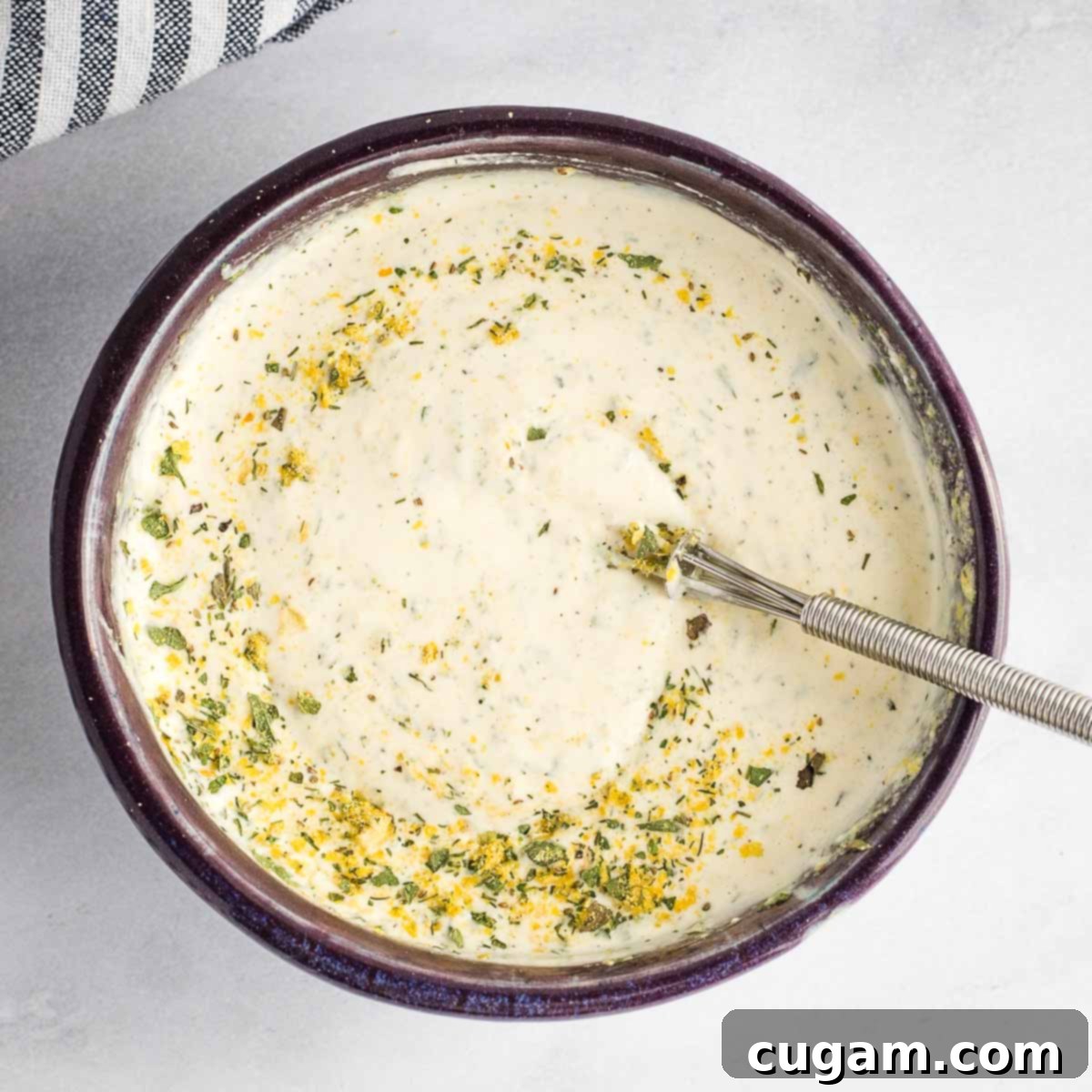 A hand whisking together ranch dip in a beautiful ceramic bowl, showing the creamy texture forming.