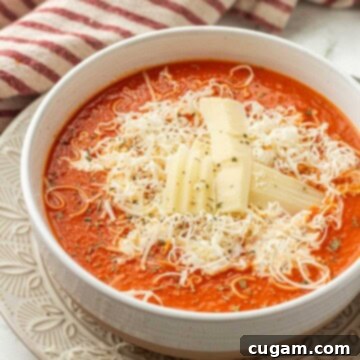 White bowl of cooked homemade bacon tomato soup in white bowl, garnished with fresh basil.