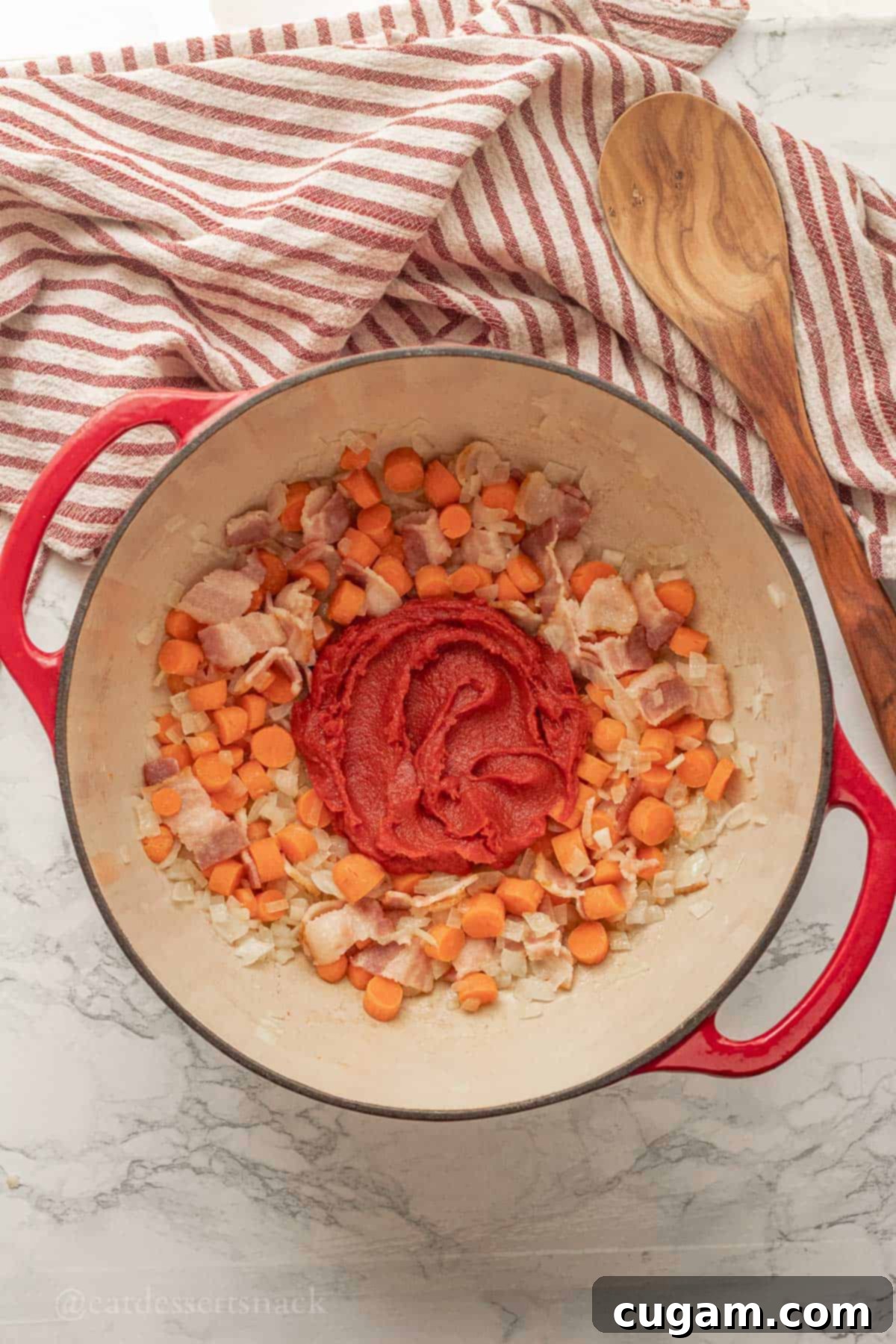 Cooked carrots, onions, and bacon in a red pot with a dollop of tomato paste, ready to be caramelized.