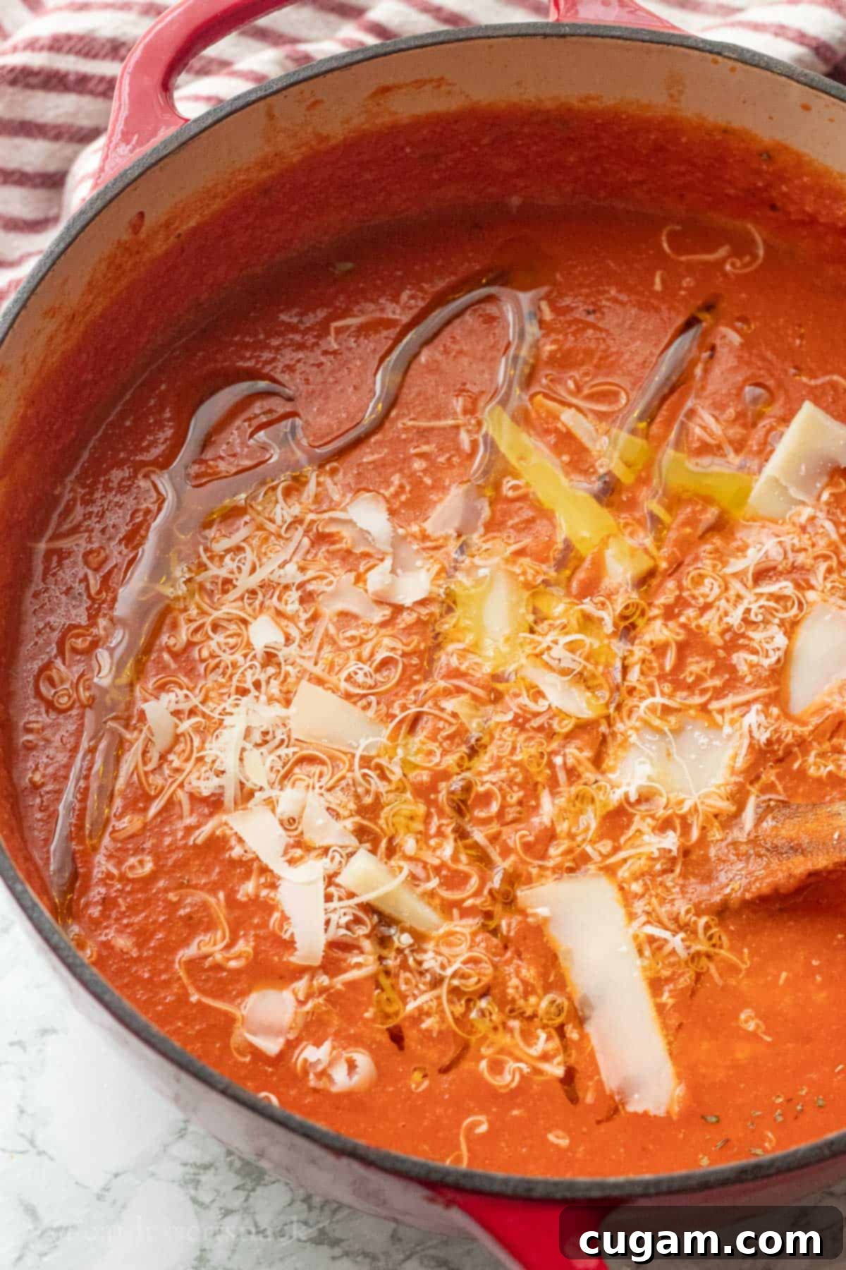 A vibrant red pot of homemade canned tomato soup, beautifully garnished with grated Parmesan cheese and a drizzle of olive oil.
