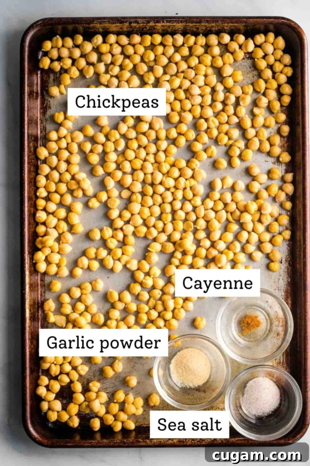 Labeled ingredients on a baking sheet: chickpeas, garlic powder, cayenne pepper, and sea salt, ready for seasoning.