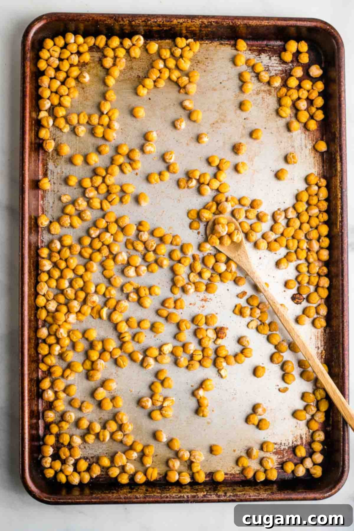 Crunchy roasted chickpeas spread out on a baking sheet, with a spoon nearby.
