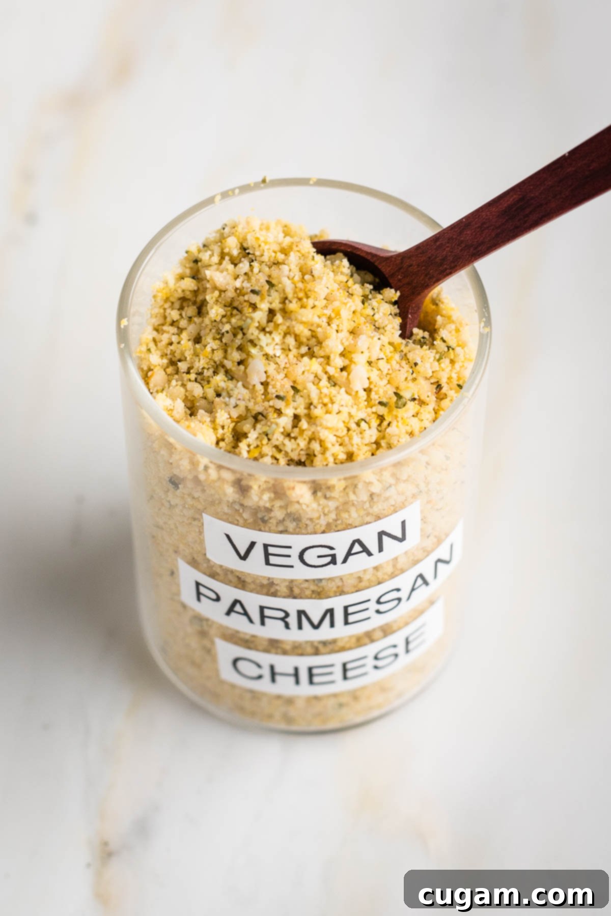 Glass spice jar labeled "vegan parmesan cheese" showing the yellow mixture with grated cheese texture from the top with a spoon.