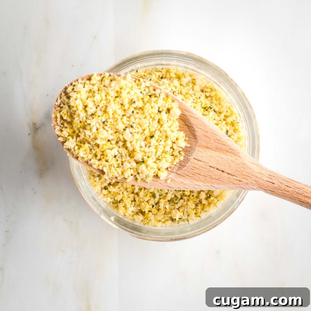 Glass jar of parmesan with a wooden spoonful of the yellow textured mix resting on top.