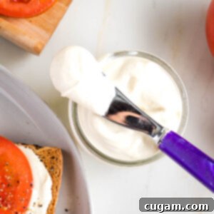 Vegan mayo in a glass jar. Purple spreader plus bright red tomatoes surround it.