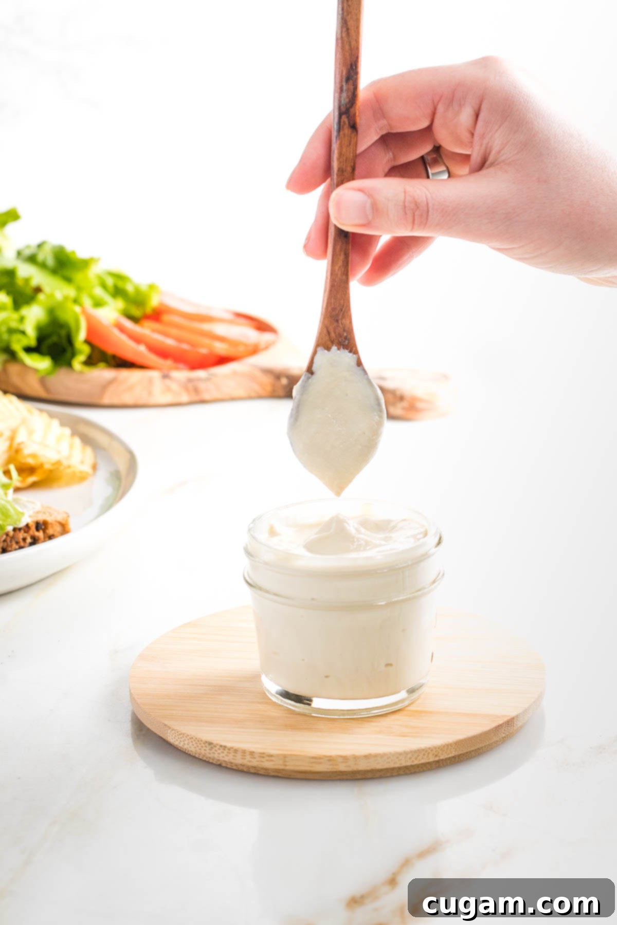Spoon showing how thick and creamy vegan mayonnaise is in a small glass mason jar.